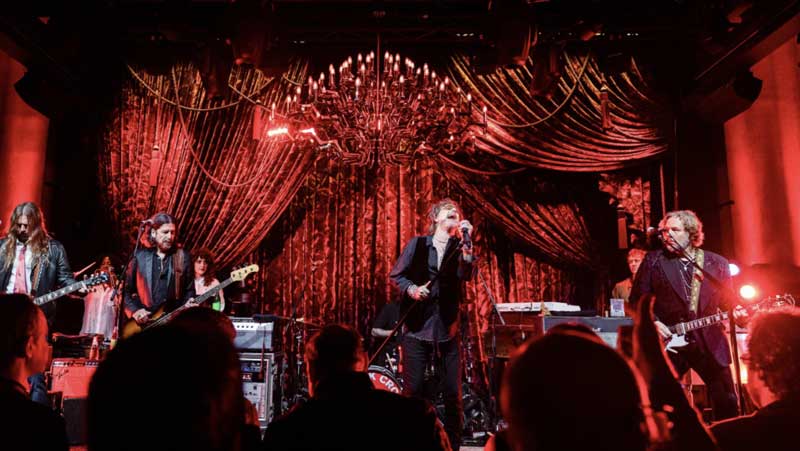 Band performing on stage with red lighting.